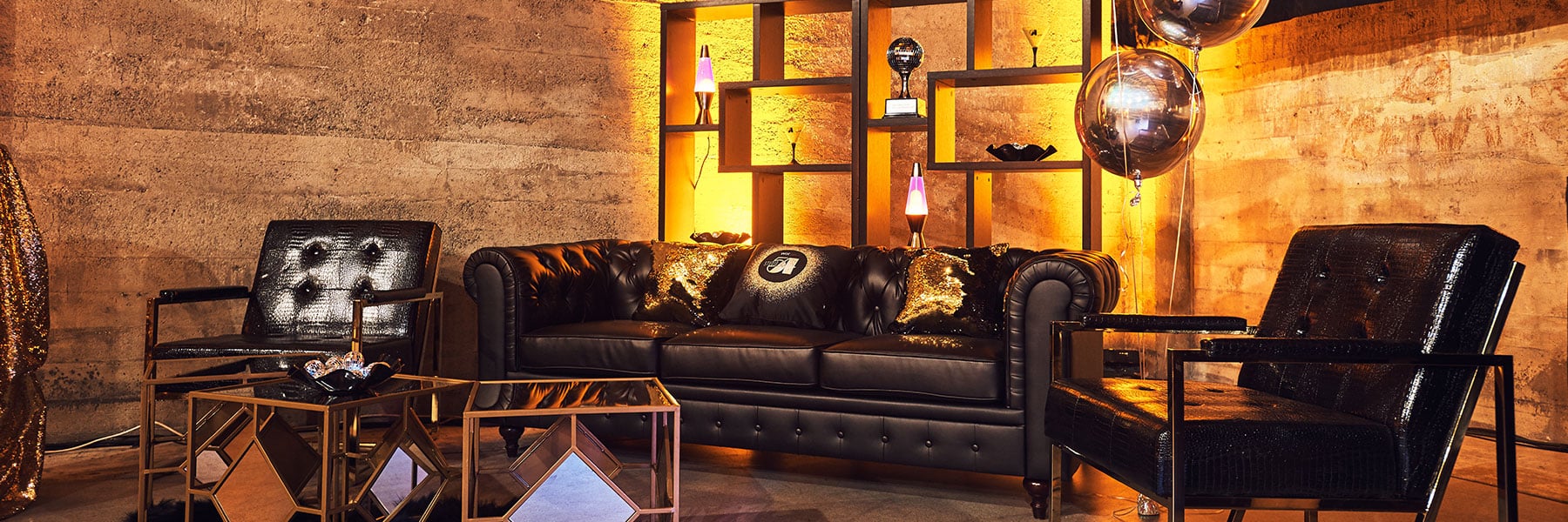 A JET lounge install: black tufted leather sofa, crocodile-texture armchairs, mirrored side tables and LED-lit shelving in a concrete event space