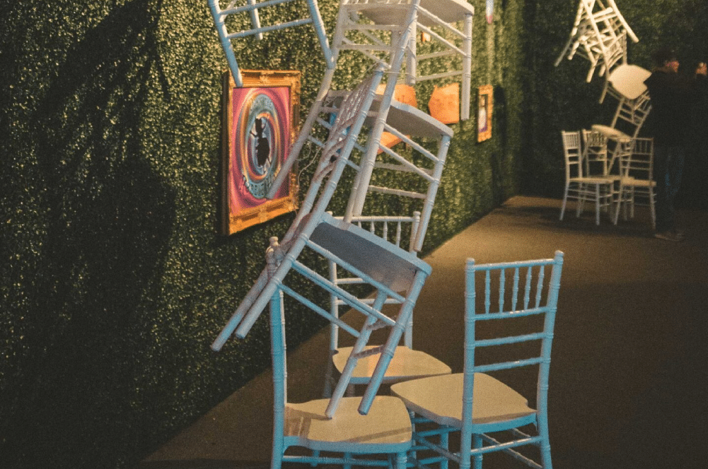 A JET chair installation: white and blue chiavari chairs mounted as a sculpture on a boxwood hedge wall at an event